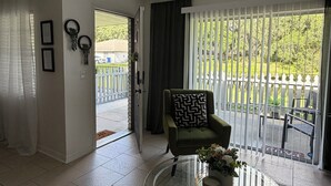 Ein Wohnzimmer mit einem Glastisch, einem grünen Sessel und Blick durch eine Glasschiebetür auf einen Außenbereich.