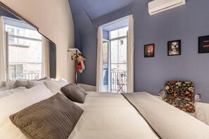A bedroom with a bed, a chair, a window, and a wall-mounted air conditioner. - tresette toledo (Naples)