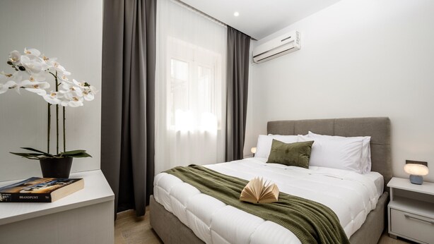 Un dormitorio moderno con una cama grande, una mesita de noche con lámpara, una planta en maceta y una ventana con cortinas.