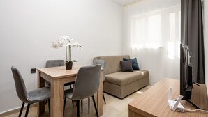 Una sala moderna con una mesa de comedor de madera, sillas tapizadas en gris, un sofá color beige, una orquídea en maceta y un dispositivo de streaming blanco sobre una mesa de madera.