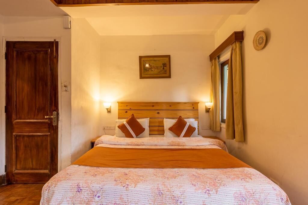 Un dormitorio con cabecera de madera, cama con colcha estampada, una puerta y un cuadro colgado en la pared.