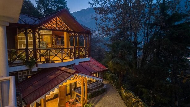 A two-story building with a balcony and a covered porch, surrounded by trees and a mountainous backdrop. - Alaya Stays The Hive Cottage (Nainital)