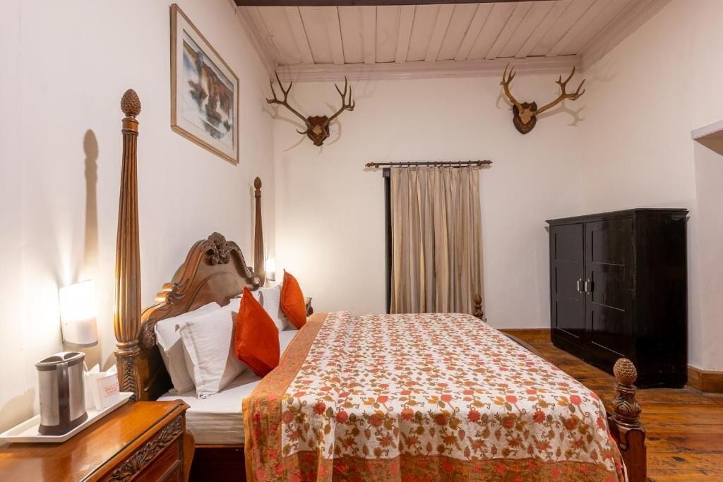 Un dormitorio con cama, mesita de noche, lámpara, cómoda y dos astas de ciervo en la pared.