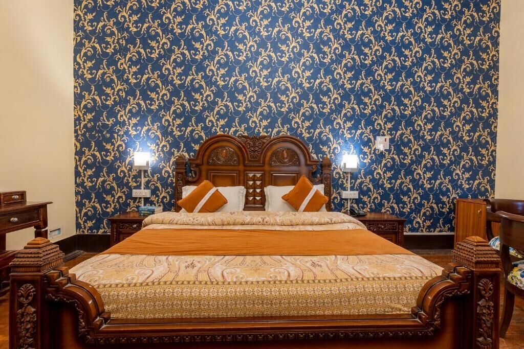 A bedroom with a large bed, ornate wooden headboard, and patterned wallpaper.