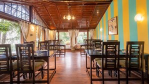 A dining area with wooden tables and chairs, large windows, and a wooden ceiling. - Alaya Stays The Hive Cottage (Nainital)