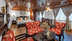 A room with a wooden ceiling, a bed with a floral bedspread, red upholstered chairs, a round table with a vase, and a window with curtains. - Alaya Stays The Hive Cottage (Nainital)