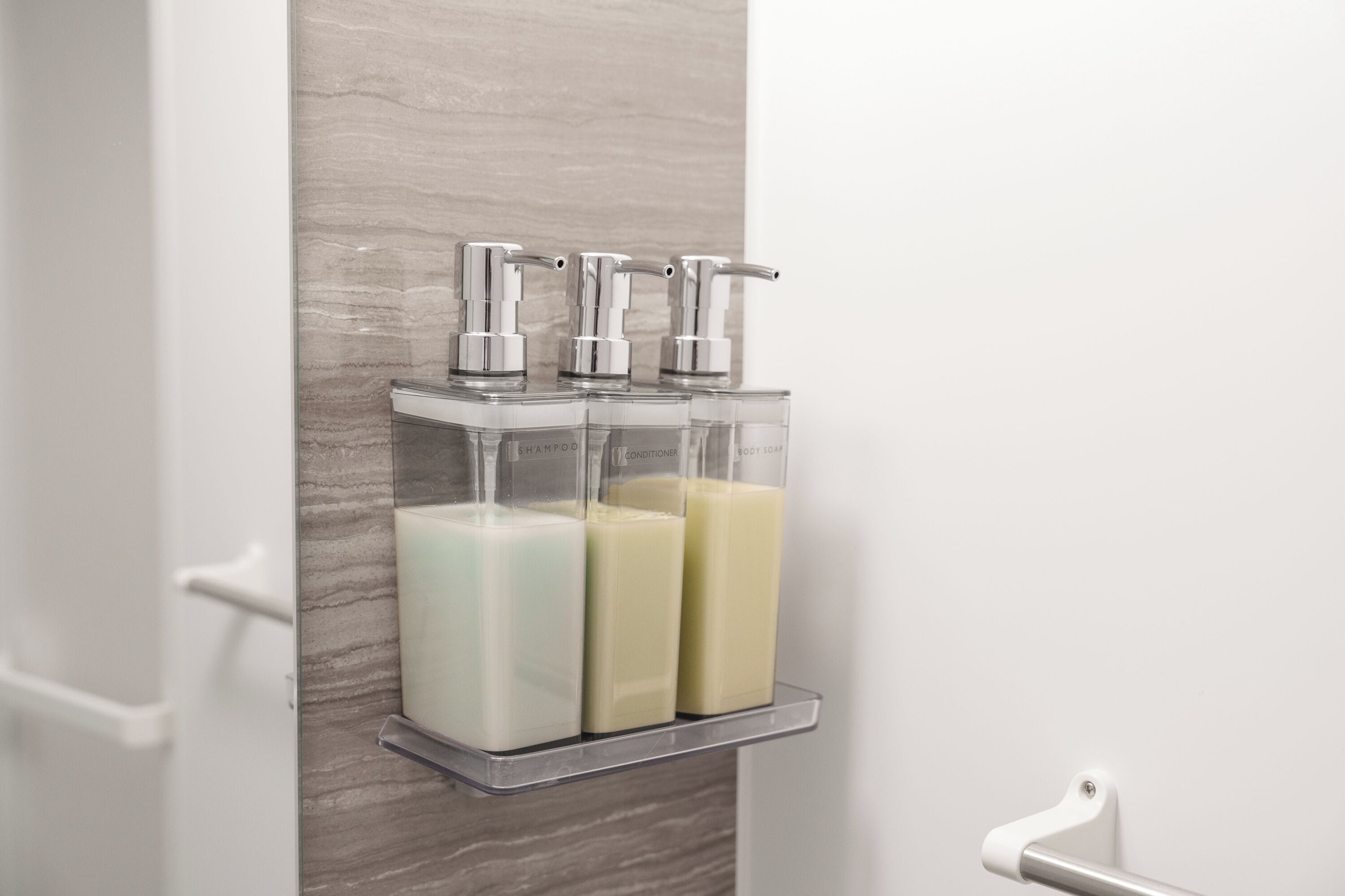 Un baño con un soporte transparente para dispensador de jabón, que contiene tres botellas de jabón.