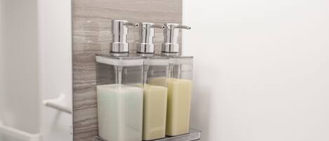 Un baño con un soporte transparente para dispensador de jabón, que contiene tres botellas de jabón.
