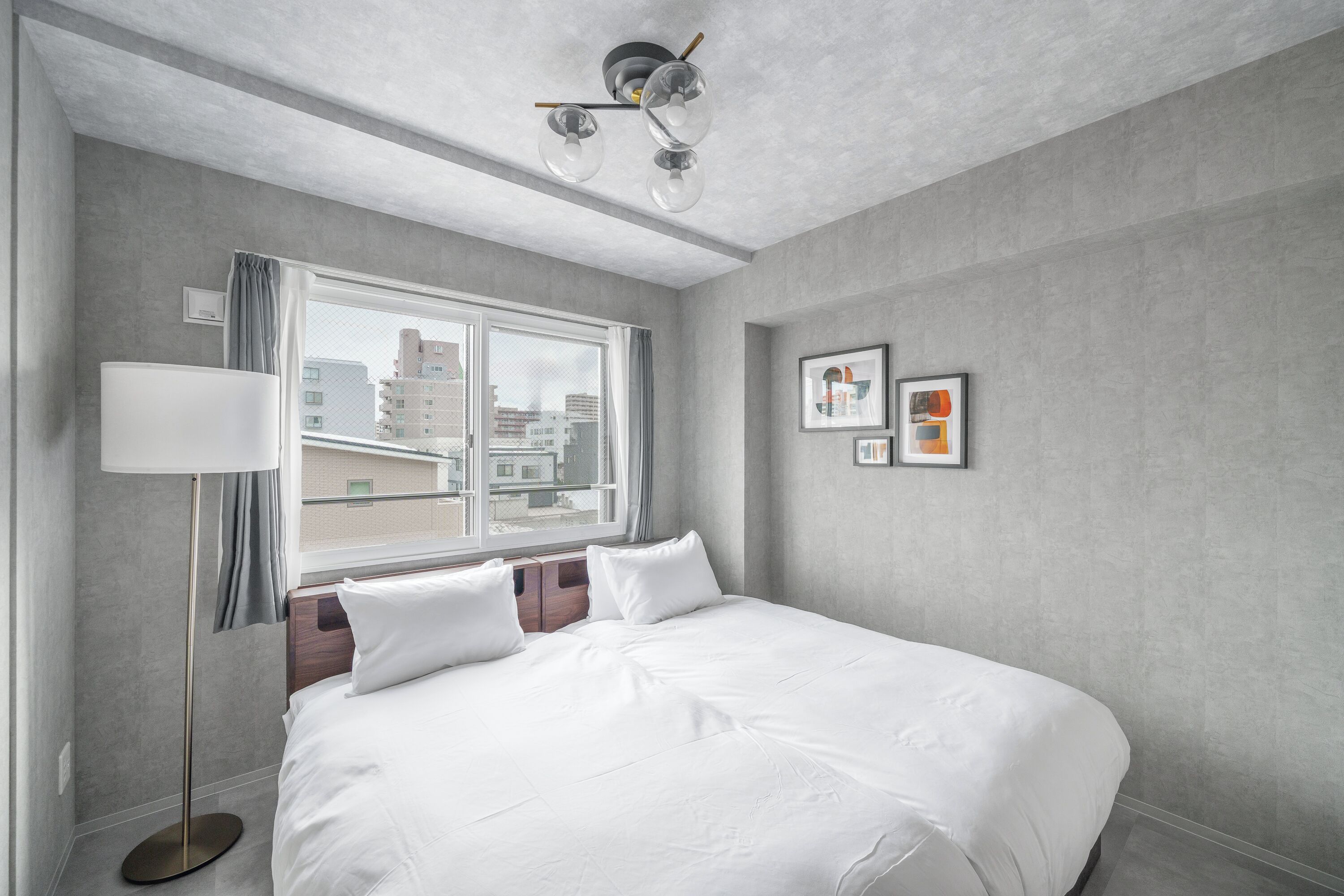 A hotel room with a large bed, a floor lamp, a window with curtains, and framed pictures on the wall.