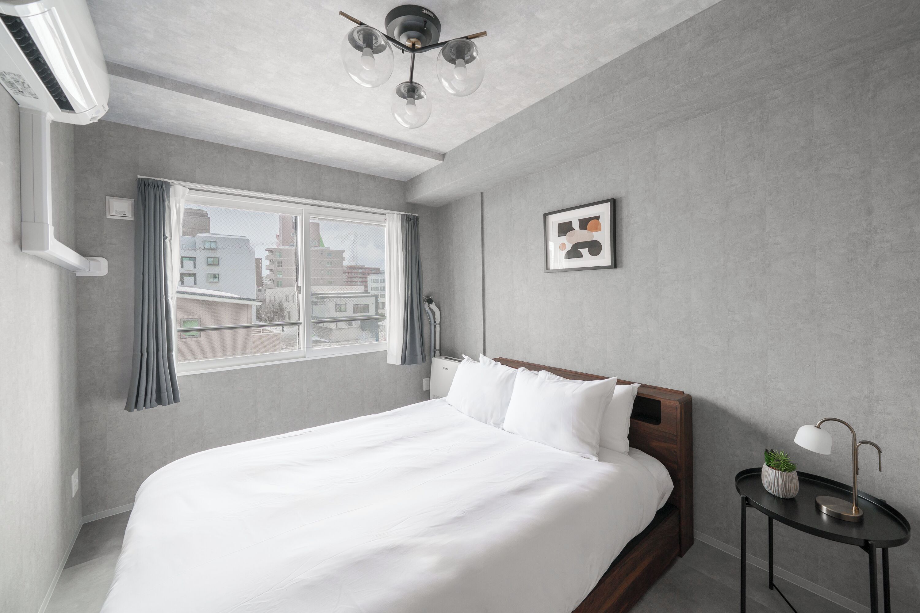 A modern hotel room with a large bed, a bedside table with a lamp, a window with curtains, and a ceiling fan.
