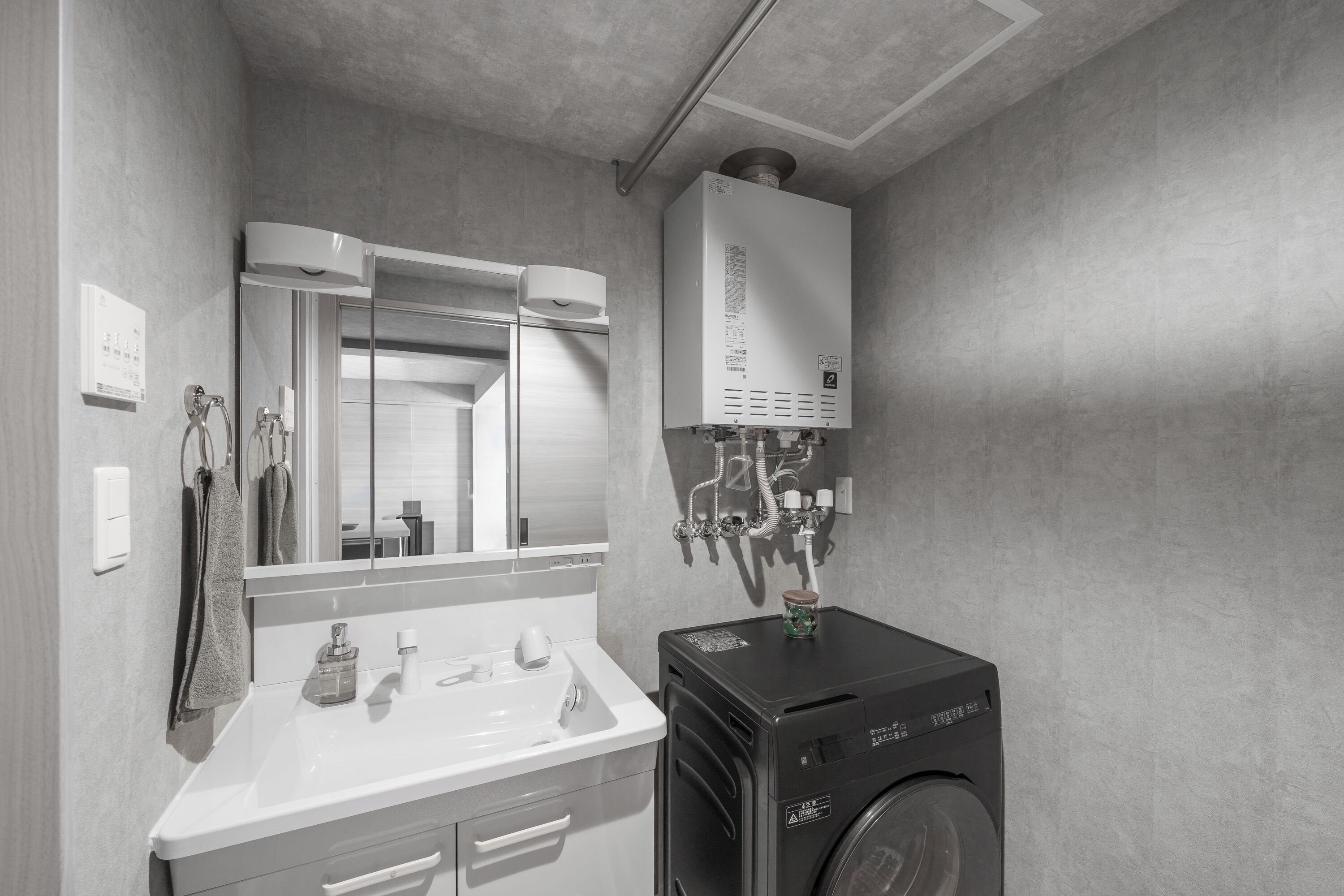 Une salle de bain moderne avec un lavabo blanc, un miroir, un porte-serviettes, un lave-linge noir et un radiateur fixé au mur.