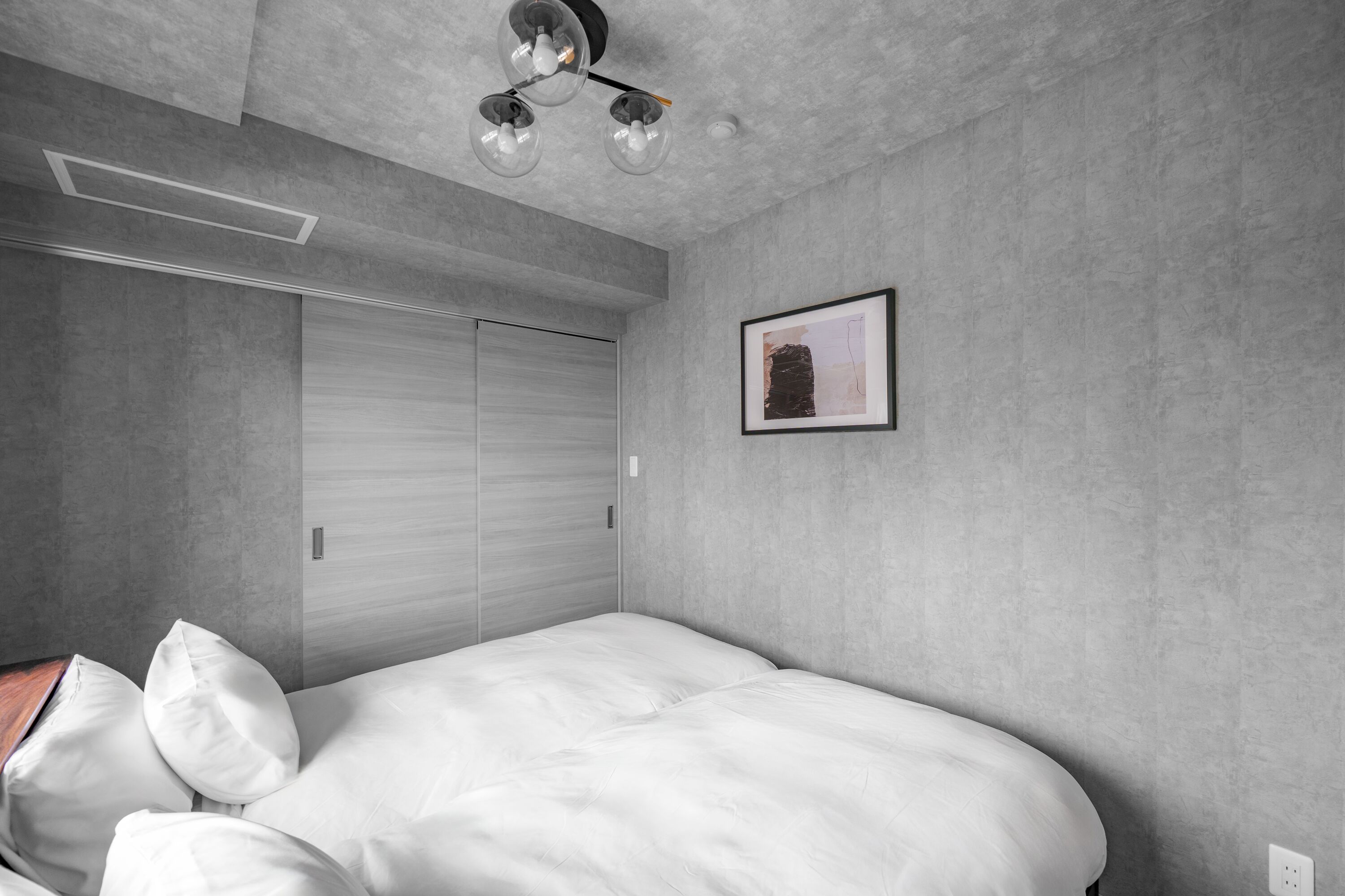 A bedroom with a bed, pillows, a framed picture, a closet, and a ceiling light fixture.