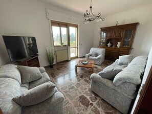A living room with a TV, two sofas, a coffee table, a chandelier, and a view through a window. - VILLA OLGA by the JONIO sea in Sud ITALIA (Marina di Ginosa)