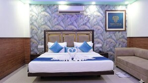 A hotel room with a bed, a ceiling fan, an air conditioning unit, a framed sign, and a sofa. - Hotel Tavooza Formely Sumangal (Gwalior)