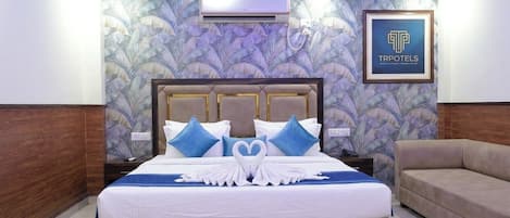 A hotel room with a bed, a ceiling fan, an air conditioning unit, a framed sign, and a sofa.