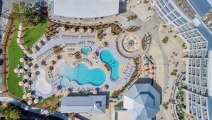 Ein Luftbild eines Hotels mit mehreren Schwimmbecken, Sitzgelegenheiten im Freien und einem angelegten Innenhof.