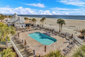Ein Poolbereich mit Liegestühlen und Sonnenschirmen, eine Laube und Blick auf den Strand.