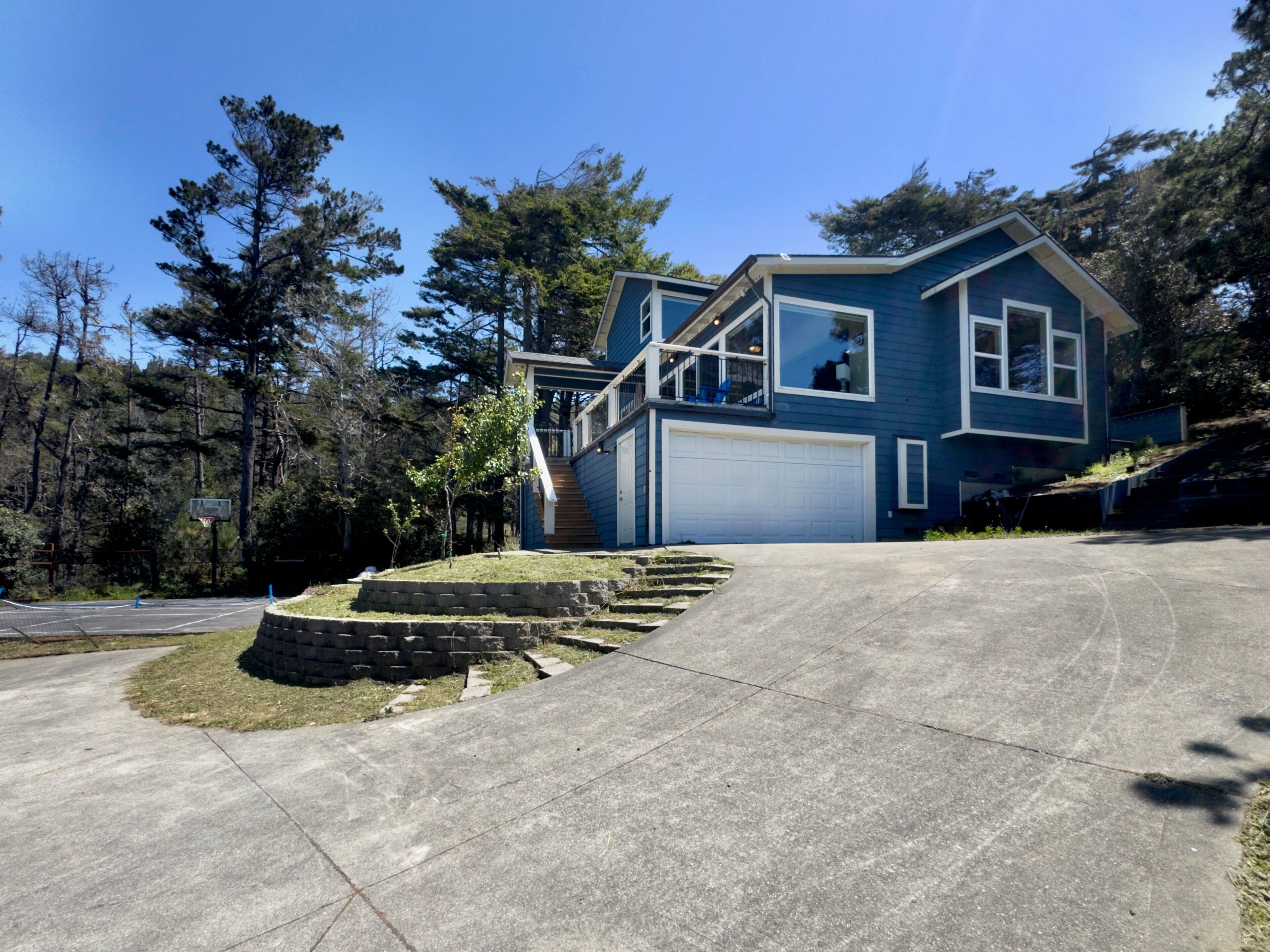 A two-story house with a garage, a front yard with a stone retaining wall, and a driveway leading to the garage.