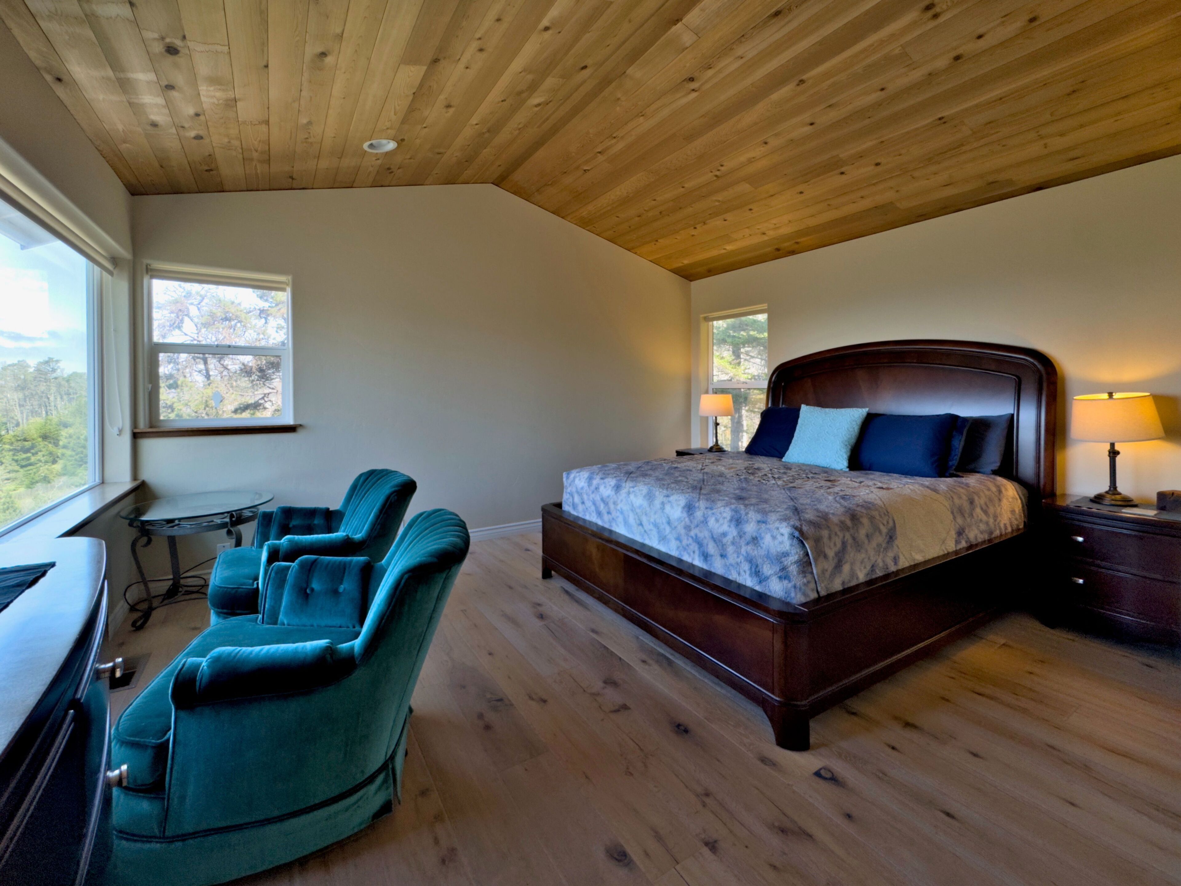 A bedroom with a wooden ceiling, a bed, a desk, and two chairs.
