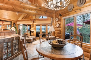 A rustic wooden interior with a dining area, wooden ceiling, and large windows.