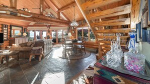 Interior de una cabaña de troncos con comedor, cocina y ventanas amplias.