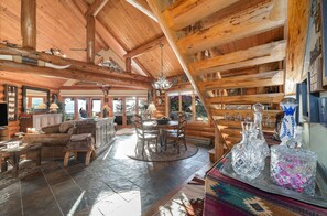A log cabin interior with a dining area, kitchen, and large windows.