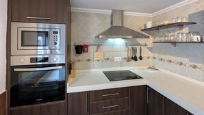 A kitchen with a microwave, oven, and stove, wooden cabinets, a tiled backsplash, and hanging utensils. - Townhouse with large terrace and mountain views in Málaga village (Villanueva del Rosario)