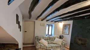 A living room with a sofa, a glass coffee table, a fireplace, and exposed wooden beams on the ceiling. - Townhouse with large terrace and mountain views in Málaga village (Villanueva del Rosario)