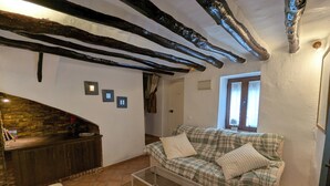 A cozy living room with exposed wooden beams, a checkered sofa, a glass coffee table, and a stone wall. - Townhouse with large terrace and mountain views in Málaga village (Villanueva del Rosario)