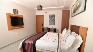 Un dormitorio con una cama, un televisor montado en la pared, una puerta y un cuadro.