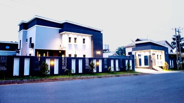 Un edificio residencial moderno de dos pisos con techo plano, balcón en el segundo nivel y entrada con portón.