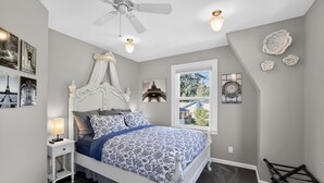 Une chambre à coucher avec un lit, une table de chevet, un ventilateur de plafond et une fenêtre donnant sur un beau paysage.