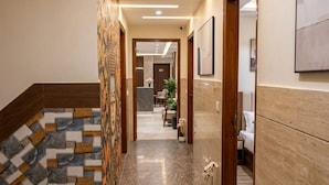 Un pasillo de hotel con suelo de mármol, puertas de madera y una recepción al fondo.