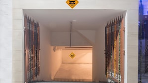 Una entrada con portón cerrado, un letrero amarillo de advertencia, una rampa de concreto y una reja metálica con detalles decorativos.
