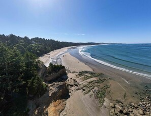 Aerial view of a sweeping sandy coastline and evergreen trees beneath a clear sky. - Depoe Bay ~ Harbor Hideaway * Hot Tub * Fireplace (Depoe Bay)