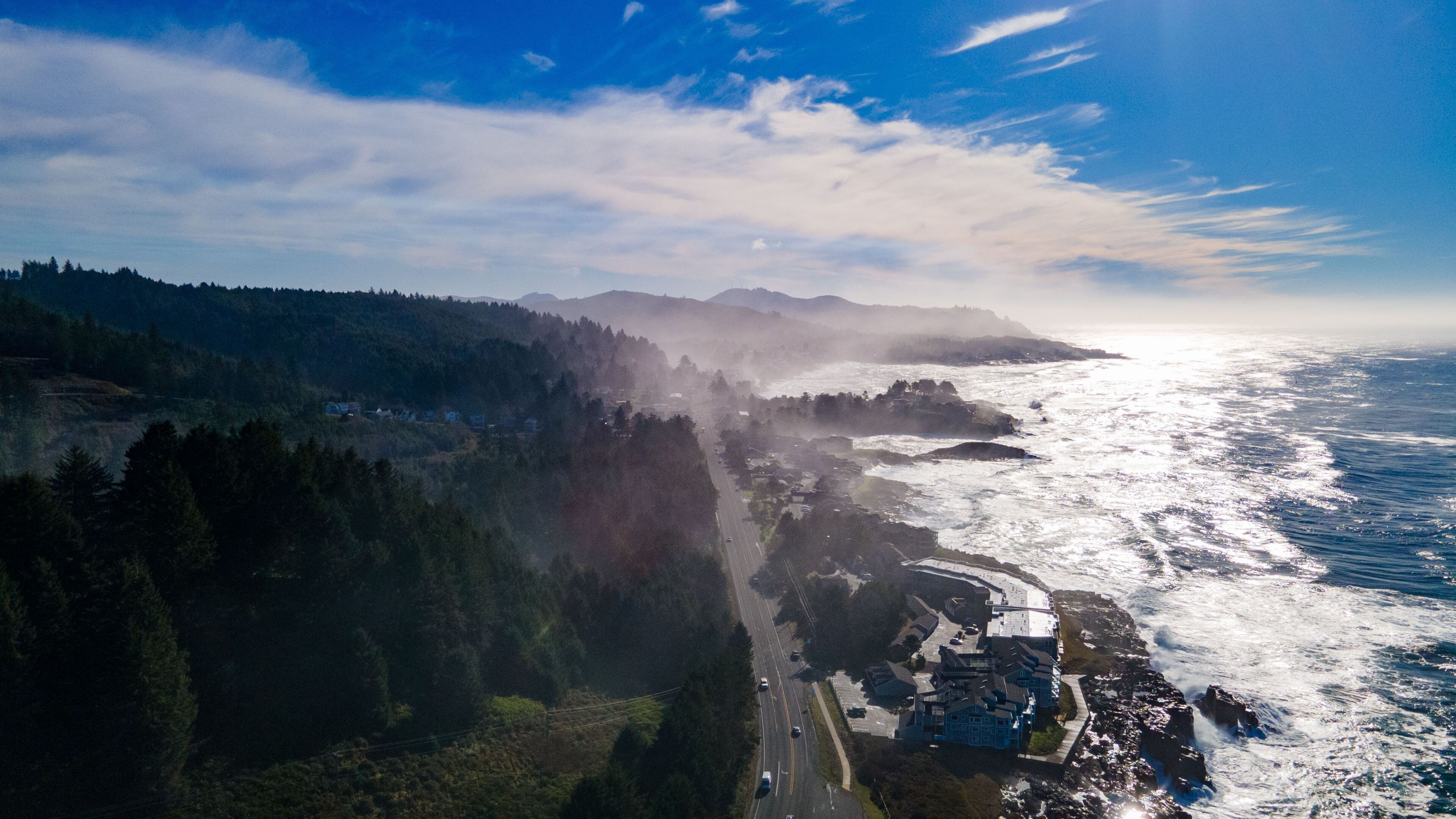 An aerial view of a coastal town with a road leading to a cliffside area, overlooking the ocean.