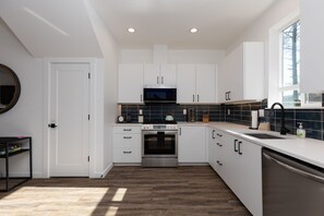 Una cocina moderna con armarios blancos, horno de acero inoxidable, microondas y lavavajillas.