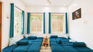 A room with a sectional sofa, two windows with curtains, a ceiling fan, and a wooden coffee table.