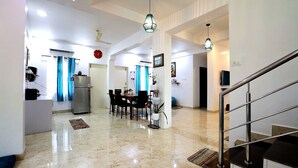 A spacious living area with a dining table, chairs, a refrigerator, and a staircase.