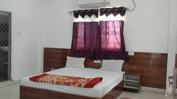 A bedroom with a wooden headboard, a bed with white bedding, two bedside tables, and purple curtains. - Hotel & Bothgaya Waterpark  (Gaya)