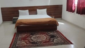 A single bed with a wooden headboard, white bedding, and a brown throw blanket. A patterned rug is on the floor. - Hotel & Bothgaya Waterpark  (Gaya)
