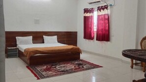 A bedroom with a bed, a small table, a chair, and a window with curtains. - Hotel & Bothgaya Waterpark  (Gaya)