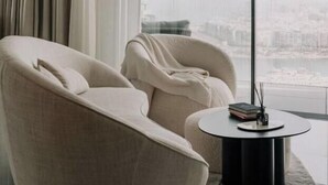 Een moderne woonkamer met een groot raam, een bank en een klein rond tafeltje met boeken.