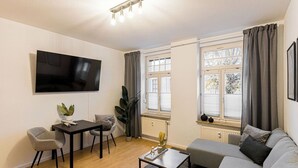 Ett vardagsrum med en platt-TV, en soffa, ett soffbord och en matplats med stolar.