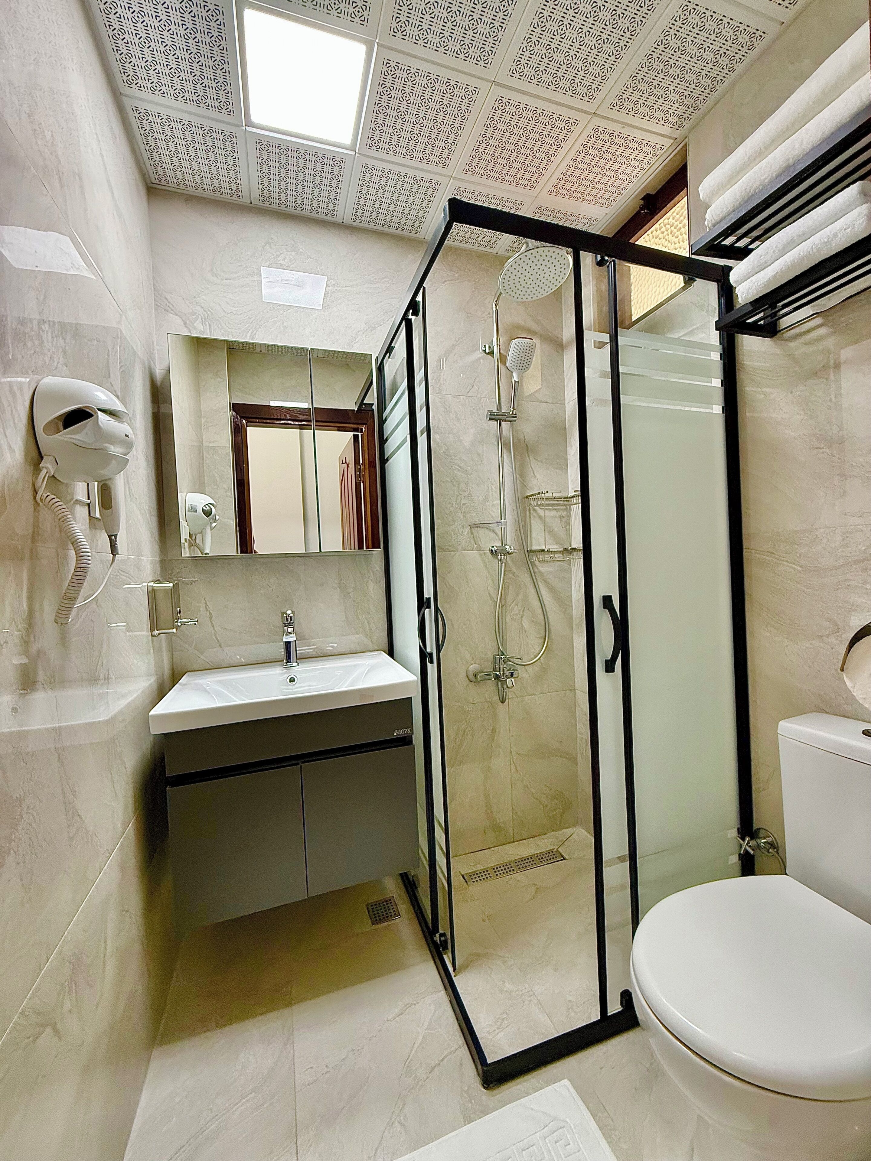 A bathroom with a glass-enclosed shower, a sink, a toilet, and a hairdryer mounted on the wall.