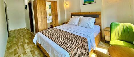A bedroom with a bed, a wooden wardrobe, a green chair, and a painting on the wall.