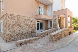 Un bâtiment doté d’une façade en pierre, d’un balcon avec une balustrade blanche et d’un escalier menant à l’entrée.