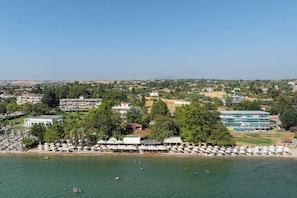 An aerial view of a coastal area with a beach, several buildings, and a large pool complex.