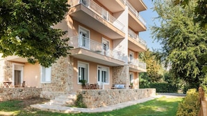 A multi-story building with balconies, stone facade, and a well-maintained lawn. - KYMA STAY - Beachfront apartments  (Thermaikos)