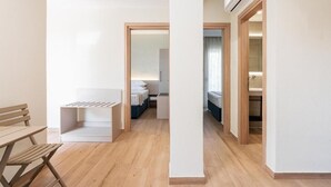 A modern, minimalist room with a wooden floor, a white desk, a bench, and a bed with a blue headboard. - KYMA STAY - Beachfront apartments  (Thermaikos)